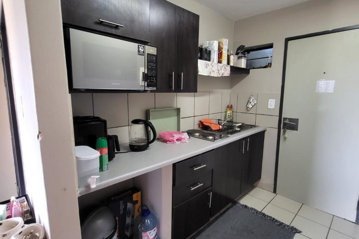 Compact kitchen featuring dark built-in cabinetry, laminate countertops, a stainless steel sink, and tiled flooring with a neutral backsplash.