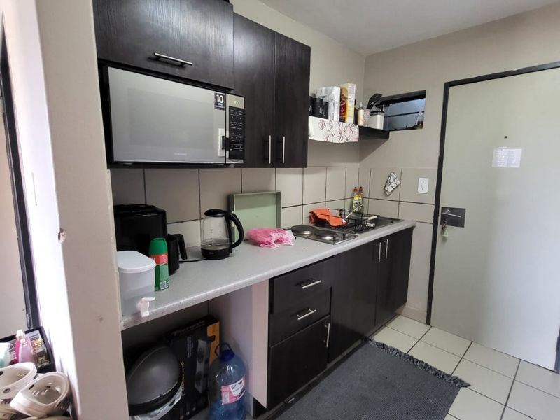Compact kitchen featuring dark built-in cabinetry, laminate countertops, a stainless steel sink, and tiled flooring with a neutral backsplash.