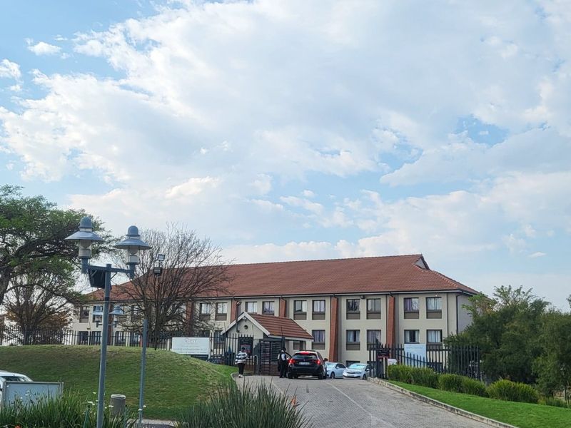 Front view of the apartment complex featuring a paved driveway, secure gated entrance, and well-maintained landscaped grounds.