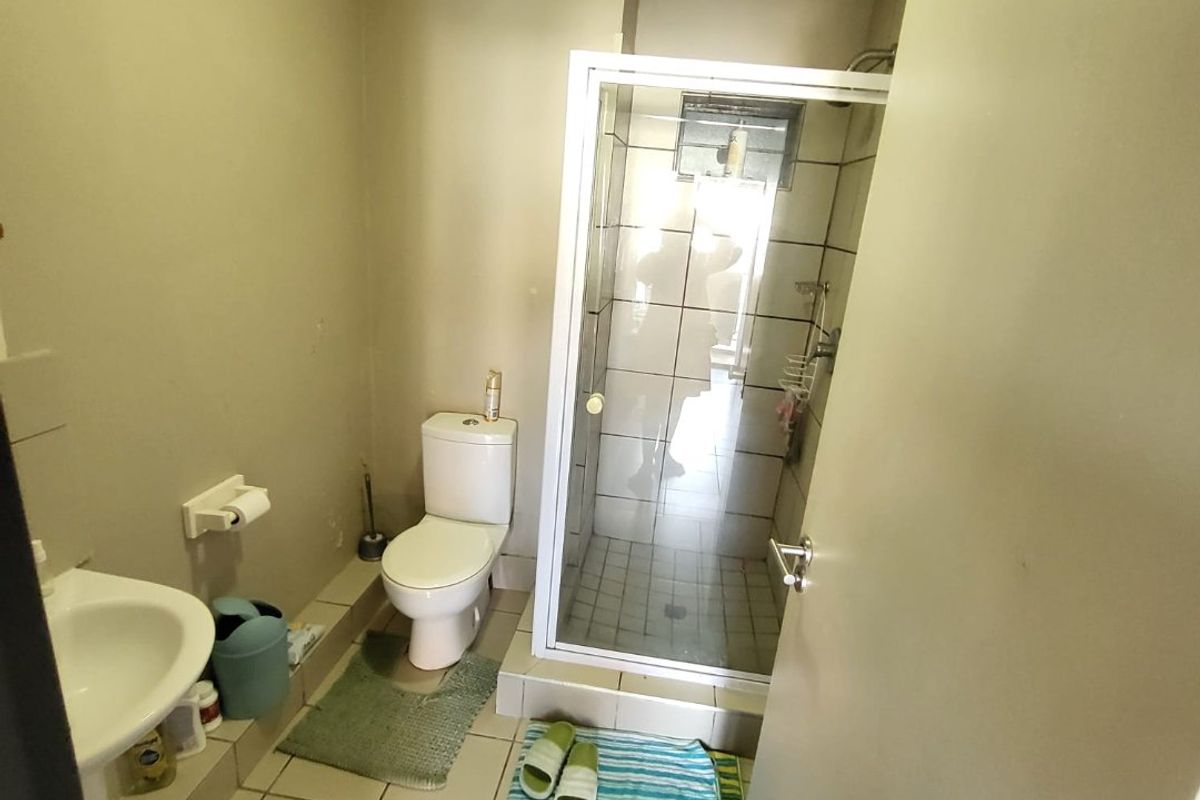 A compact bathroom featuring a shower enclosure, pedestal basin, and toilet with tiled flooring. The space shows signs of wear and requires cosmetic updates.