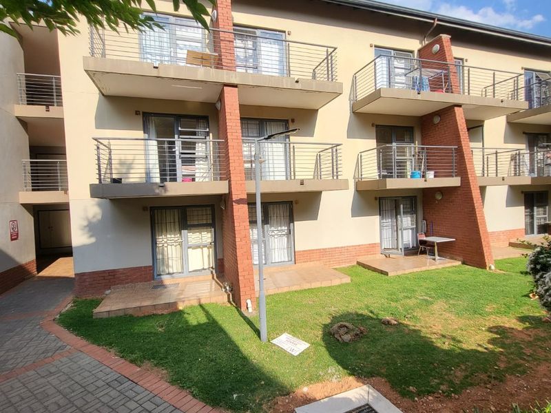 Rear view of a multi-story apartment complex featuring private balconies, ground-floor patios, and a shared garden area with brick and plaster facade finishes.