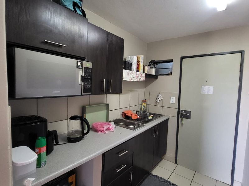 Compact kitchen featuring dark wood-finish cabinetry, light laminate countertops, a built-in microwave, and tiled flooring with a functional layout.