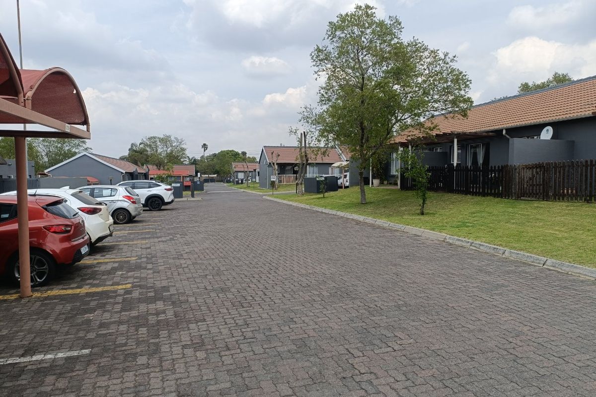 A view of the townhouse complex street, featuring paved driveways, covered carports, and well-maintained residential units with tiled roofs.