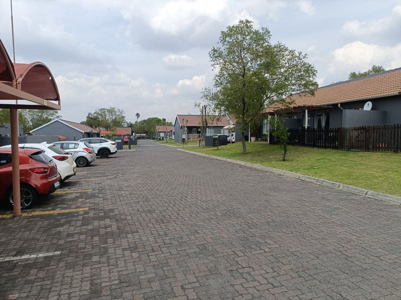 A view of the townhouse complex street, featuring paved driveways, covered carports, and well-maintained residential units with tiled roofs.