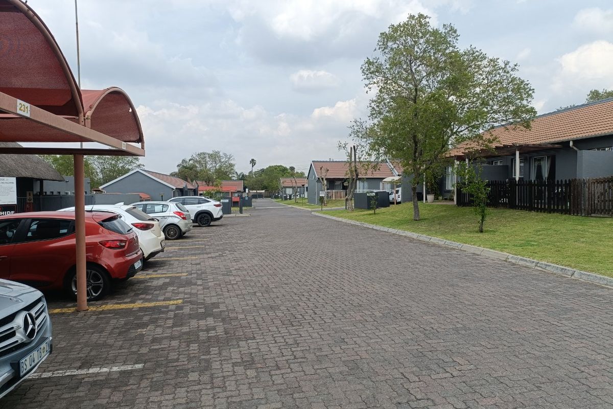 A view of the townhouse complex street, featuring paved driveways, covered parking bays, and well-maintained residential units with tiled roofs.