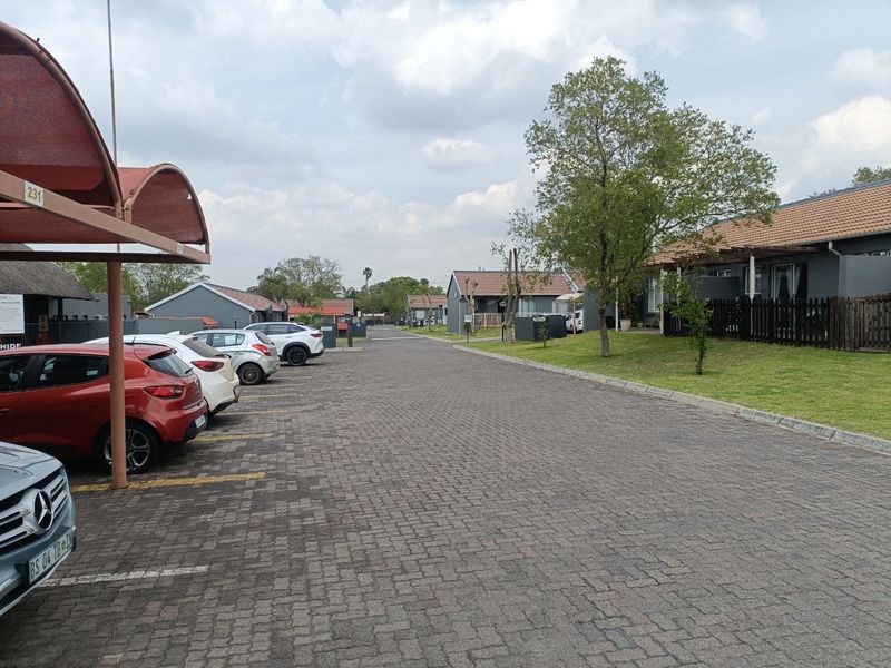 A view of the townhouse complex street, featuring paved driveways, covered parking bays, and well-maintained residential units with tiled roofs.