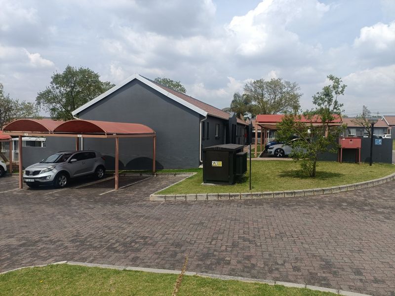 Exterior view of a townhouse complex featuring a paved driveway, covered carports, and well-maintained lawn areas.