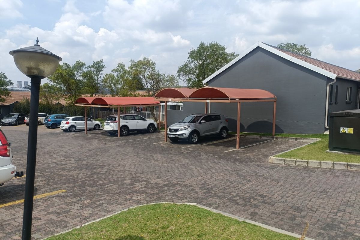 A well-maintained townhouse complex exterior featuring paved parking areas, covered carports, and neat lawn landscaping.