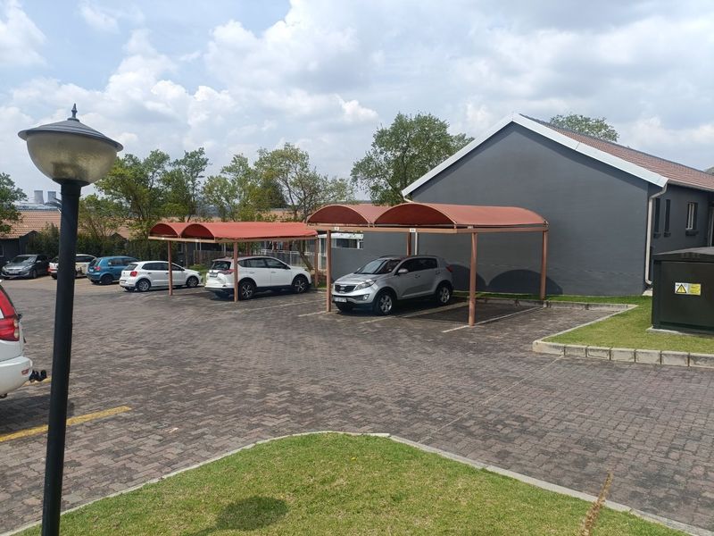 A well-maintained townhouse complex exterior featuring paved parking areas, covered carports, and neat lawn landscaping.