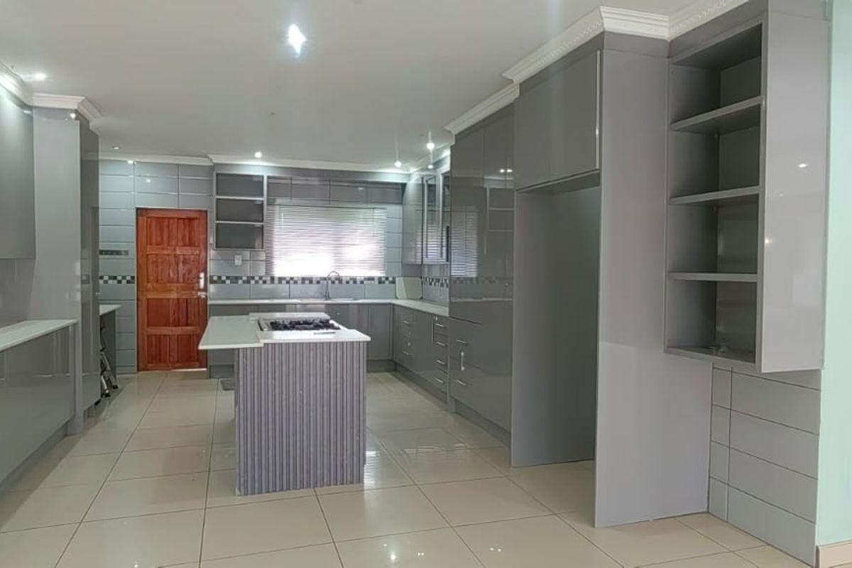 Modern kitchen featuring sleek grey cabinetry, a central island with a built-in gas hob, tiled flooring, and contemporary finishes throughout.