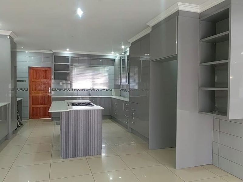 Modern kitchen featuring sleek grey cabinetry, a central island with a built-in gas hob, tiled flooring, and contemporary finishes throughout.