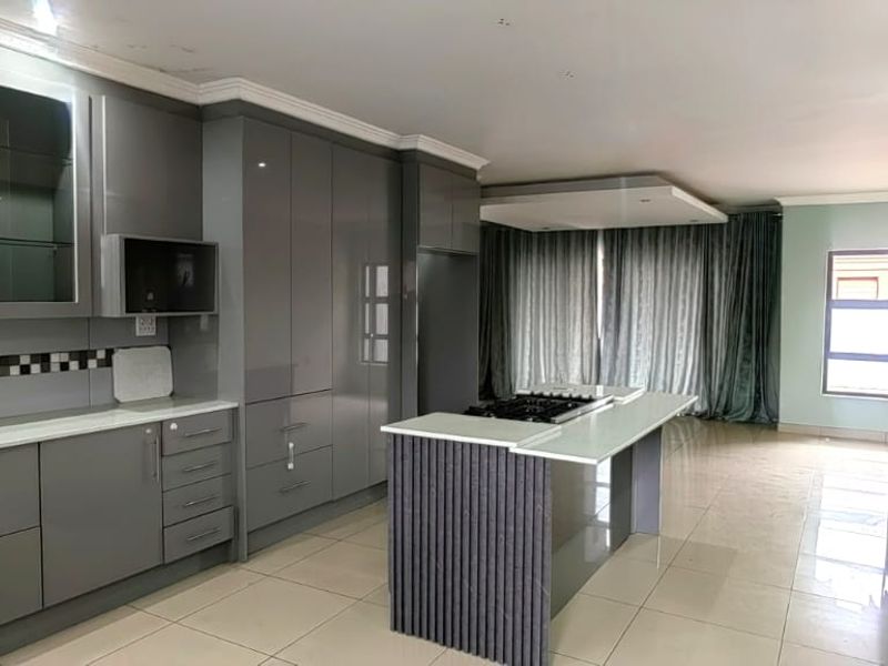 Modern kitchen featuring sleek grey cabinetry, a central island with a built-in hob, and tiled flooring, offering a clean and contemporary aesthetic.