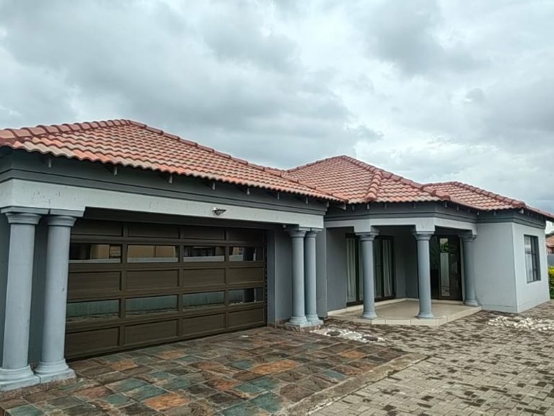 A well-maintained single-story house featuring a tiled roof, decorative columns, a paved driveway, and a double garage.