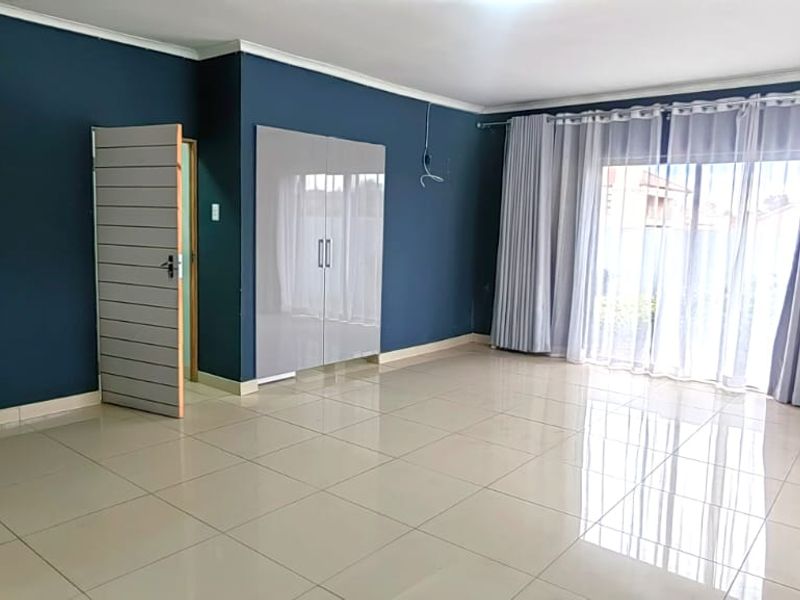 Spacious bedroom featuring dark blue accent walls, neutral tiled flooring, built-in cupboards, and large sliding doors providing access to the exterior.
