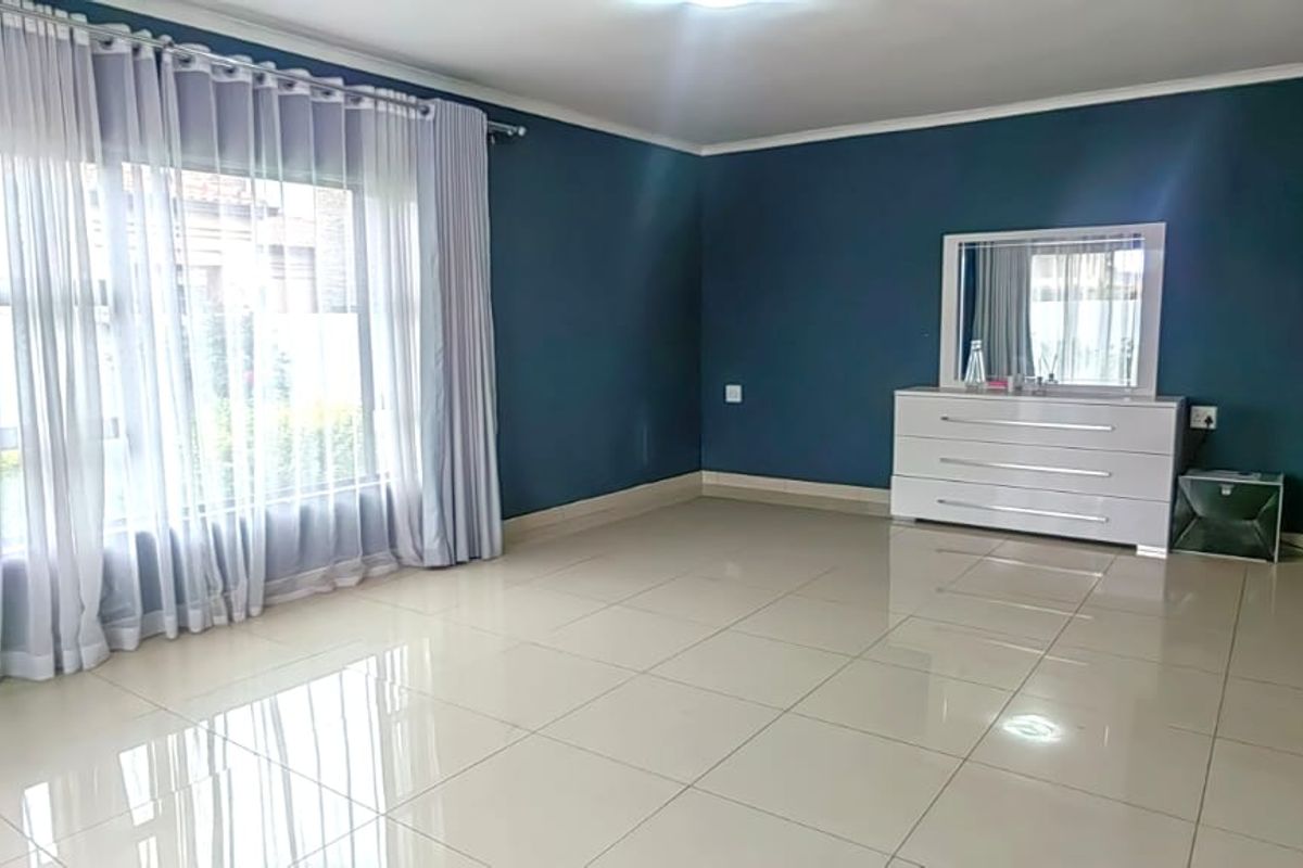 Spacious bedroom featuring polished tiled flooring, neutral cove cornicing, and large windows with curtains, providing a bright and well-maintained living space.