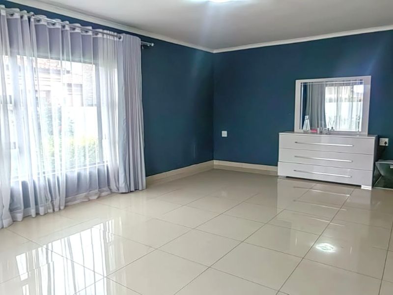 Spacious bedroom featuring polished tiled flooring, neutral cove cornicing, and large windows with curtains, providing a bright and well-maintained living space.