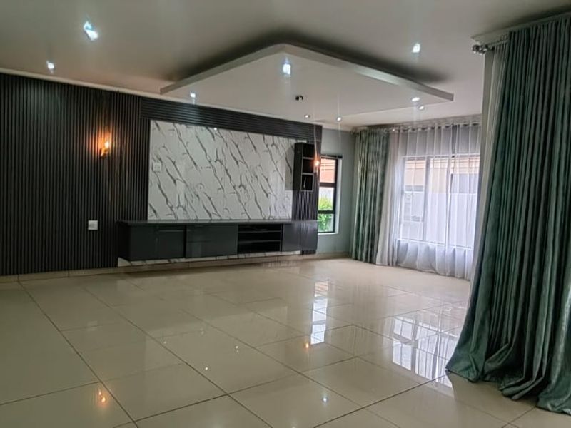 Spacious living room featuring a modern built-in media unit, marble-look feature wall, recessed ceiling with downlights, and large sliding doors leading to the exterior.