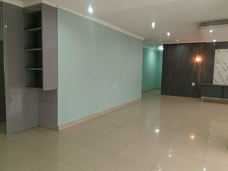Spacious open-plan living area featuring modern grey cabinetry, sleek tiled flooring, and a contemporary feature wall with integrated lighting.