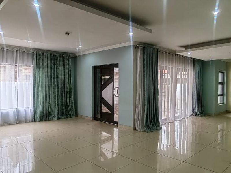Spacious, light-filled living area featuring modern recessed ceilings, downlights, and large windows with tiled flooring throughout.