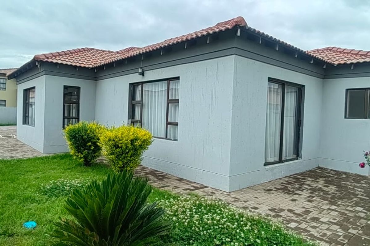 Rear view of the house featuring a paved patio area, terracotta roof tiles, and aluminium-framed windows and sliding doors.