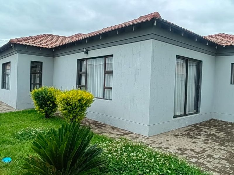 Rear view of the house featuring a paved patio area, terracotta roof tiles, and aluminium-framed windows and sliding doors.