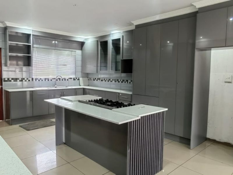 Modern kitchen featuring sleek grey cabinetry, a central island with a gas hob, tiled flooring, and a tiled backsplash.