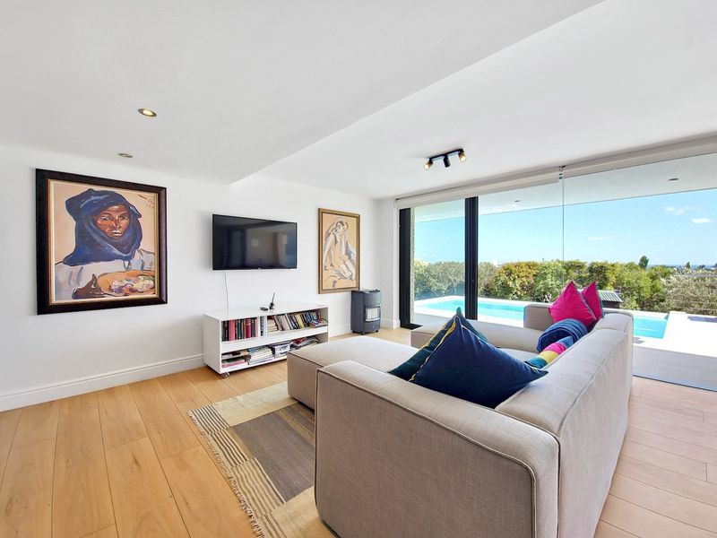 A bright, modern living room featuring timber flooring, recessed lighting, and large sliding glass doors that open onto a pool area with scenic views.