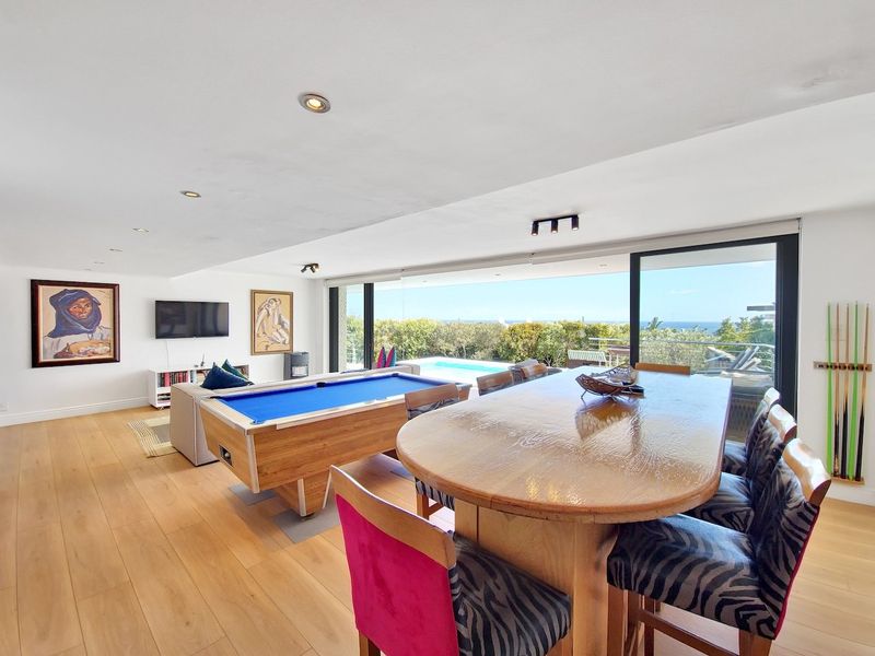 Spacious open-plan living and dining area featuring hardwood floors, recessed lighting, and large sliding glass doors opening to a pool deck with ocean views.