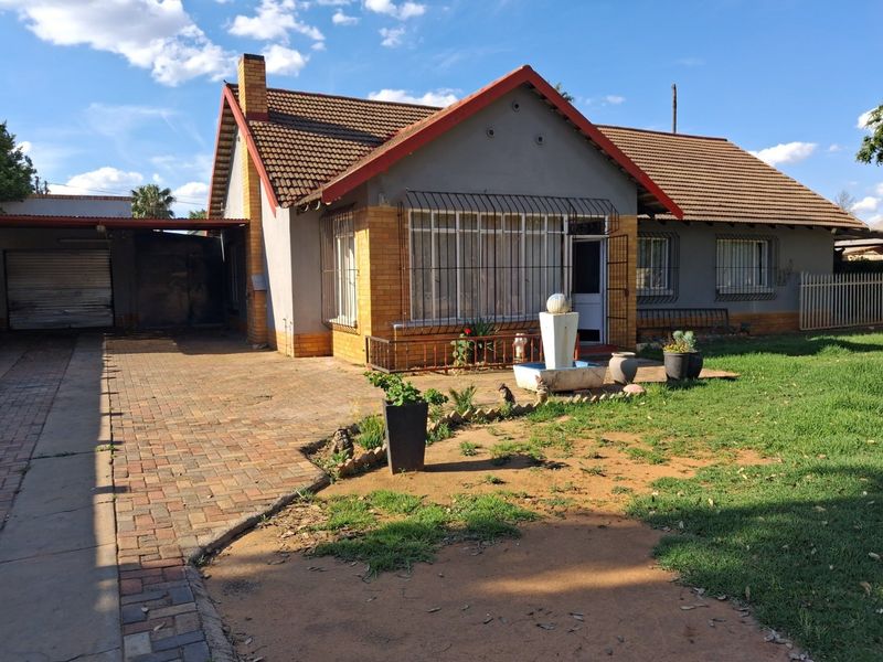 Front view of a single-story house featuring a brick driveway, attached carport, tiled roof, and security bars on windows.