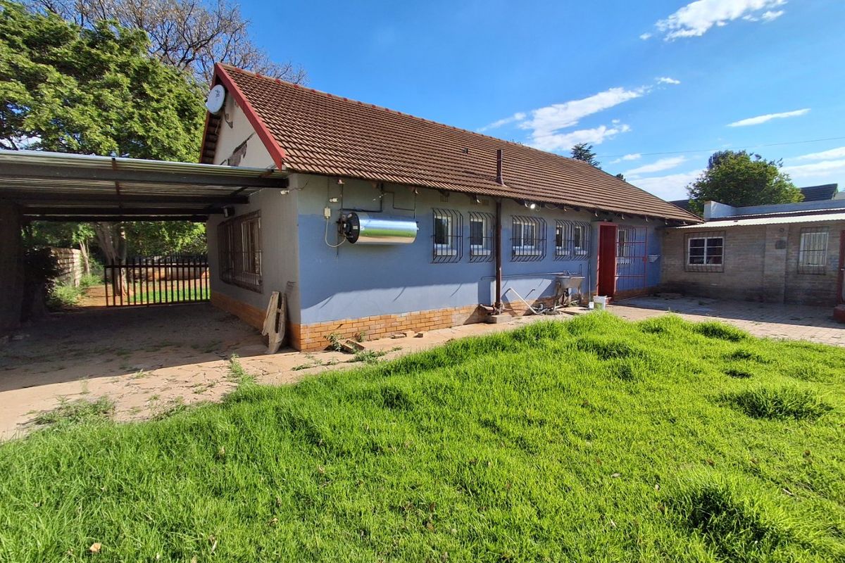 Rear view of the house featuring a tiled roof, attached carport, solar geyser, and security bars on windows, set against a large garden area.
