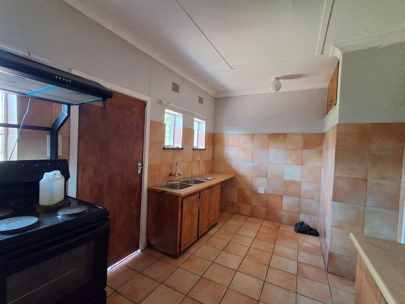 A functional kitchen featuring built-in wooden cabinetry, a double sink, tiled splashbacks, and tiled flooring, offering a blank canvas for potential renovation.