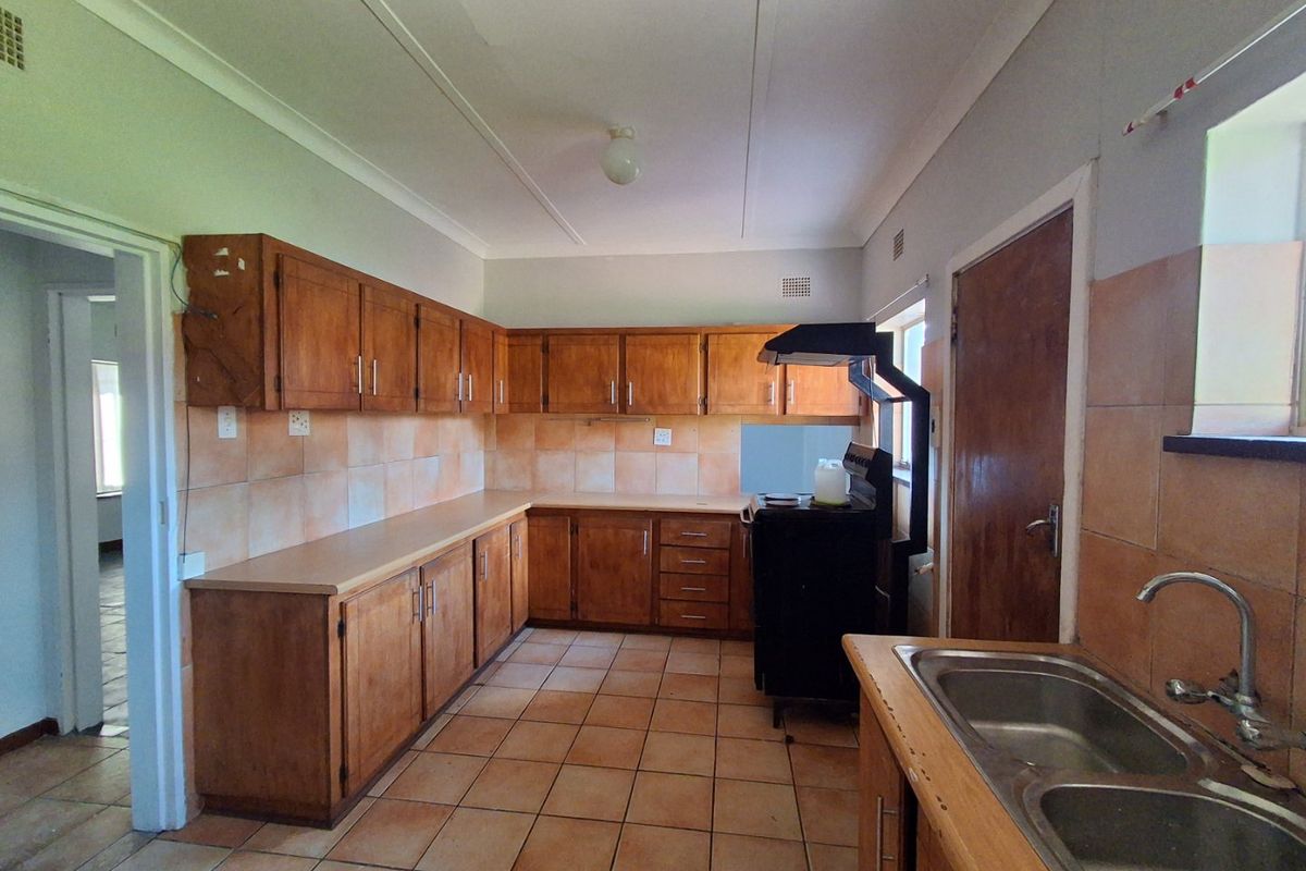 A functional kitchen featuring wooden cabinetry, laminate countertops, a double bowl sink, and tiled finishes throughout, offering potential for modern renovation.