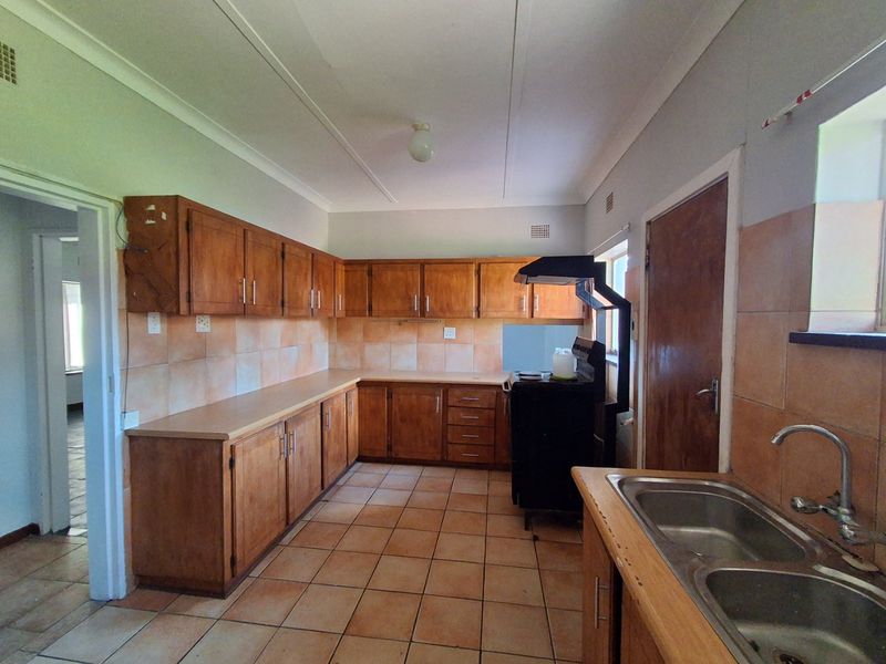A functional kitchen featuring wooden cabinetry, laminate countertops, a double bowl sink, and tiled finishes throughout, offering potential for modern renovation.