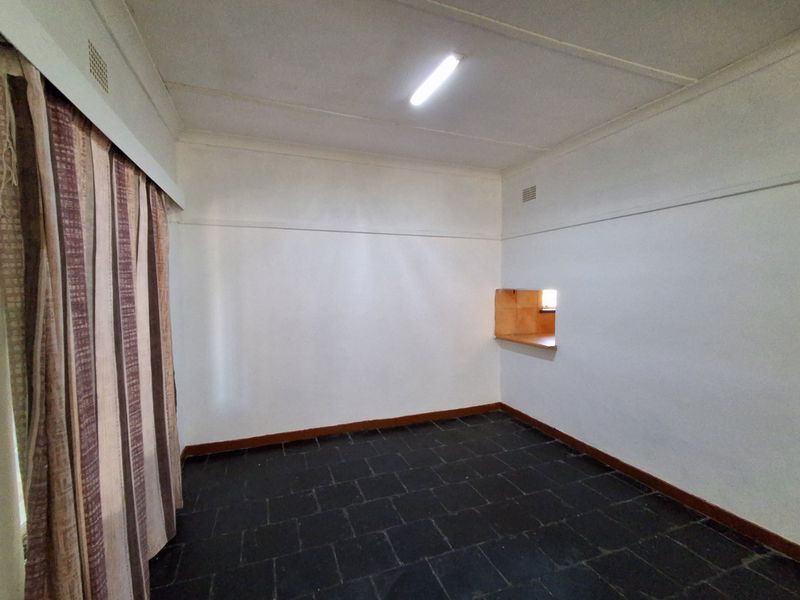 An empty living area featuring dark tiled flooring, a serving hatch to the kitchen, and basic ceiling lighting.