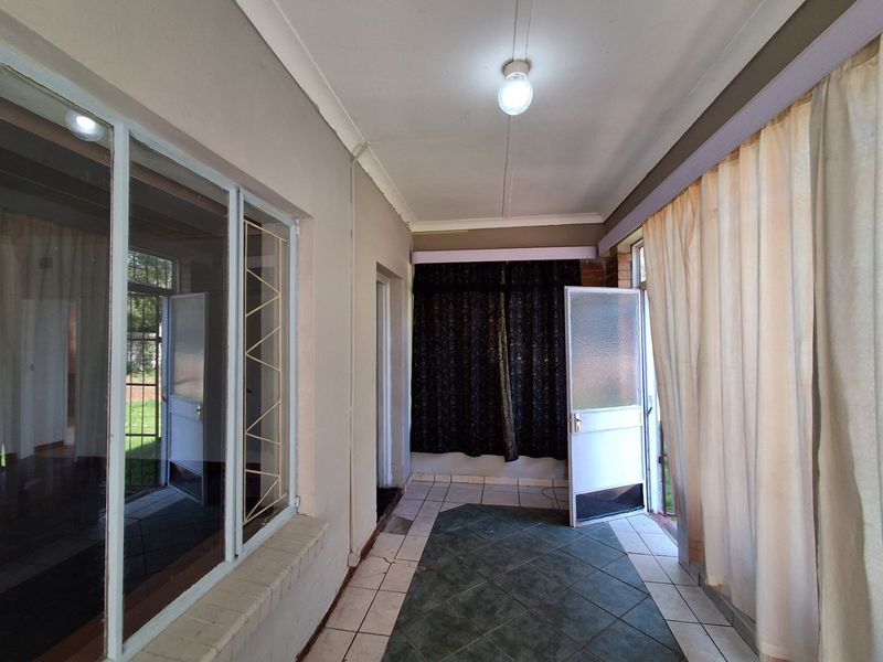 A covered patio area featuring tiled flooring, large windows, and direct access to the garden, offering a versatile space for outdoor living.