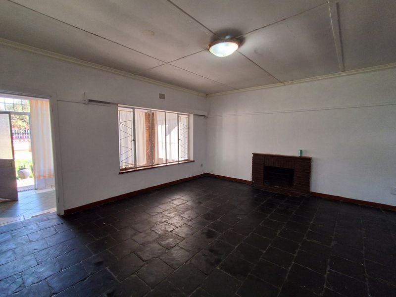 An empty living room featuring dark slate tile flooring, a brick fireplace, and access to an outdoor area through a security gate.