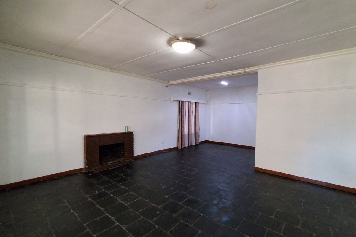 An empty living room featuring a brick fireplace, dark stone tile flooring, and a classic ceiling design, offering a blank canvas for renovation.