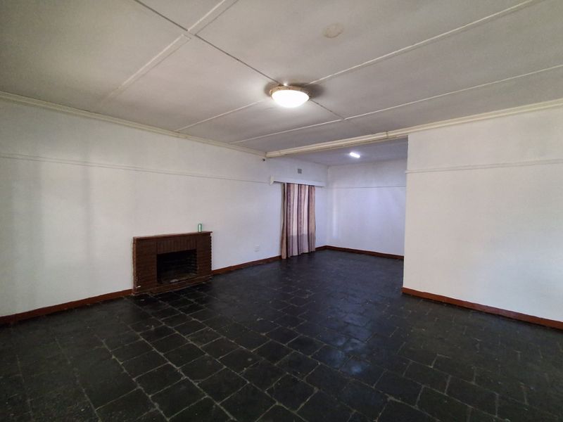 An empty living room featuring a brick fireplace, dark stone tile flooring, and a classic ceiling design, offering a blank canvas for renovation.