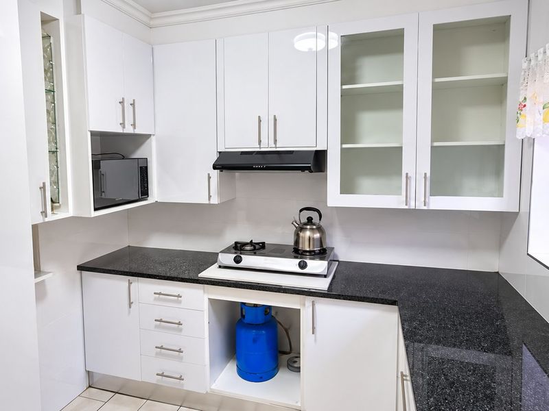 A functional kitchen featuring white cabinetry, black granite countertops, a gas hob, and an extractor fan, with a window providing natural light.