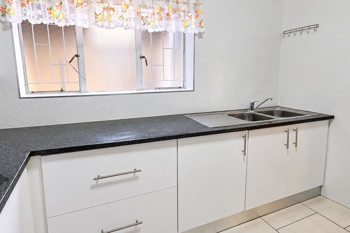A clean and functional kitchen featuring white cabinetry, dark granite countertops, a stainless steel double sink, and tiled flooring.