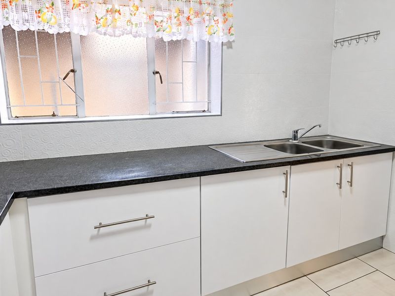 A clean and functional kitchen featuring white cabinetry, dark granite countertops, a stainless steel double sink, and tiled flooring.