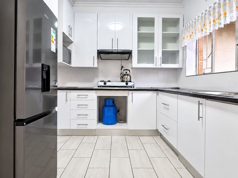 A modern, well-maintained kitchen featuring white cabinetry, black granite countertops, a gas hob with extractor, and tiled flooring.