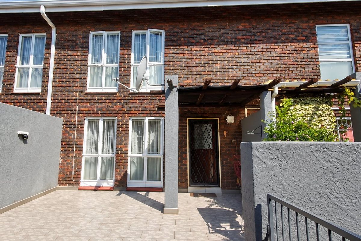 Rear exterior view of a townhouse featuring a brick facade, a tiled patio area, and a timber pergola structure.