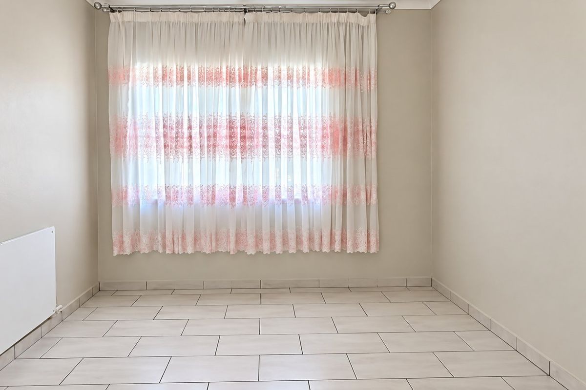A clean, empty bedroom featuring neutral wall paint, tiled flooring, and a wall-mounted electric heater, ready for personalization.