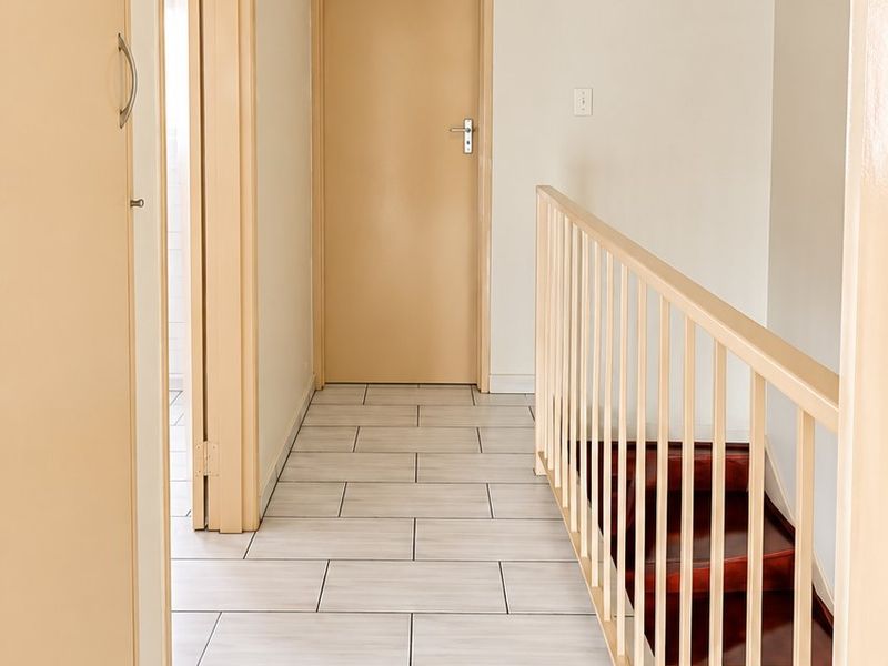 A bright, clean hallway featuring light-toned tiled flooring, built-in storage cupboards, and a staircase with a simple balustrade.