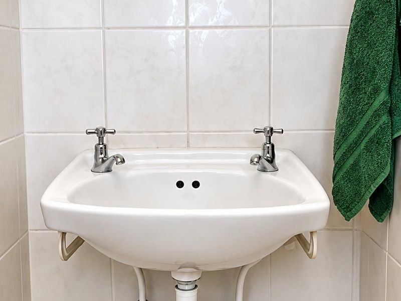 A compact bathroom featuring a wall-mounted ceramic basin with chrome taps, tiled walls, and a wooden medicine cabinet.