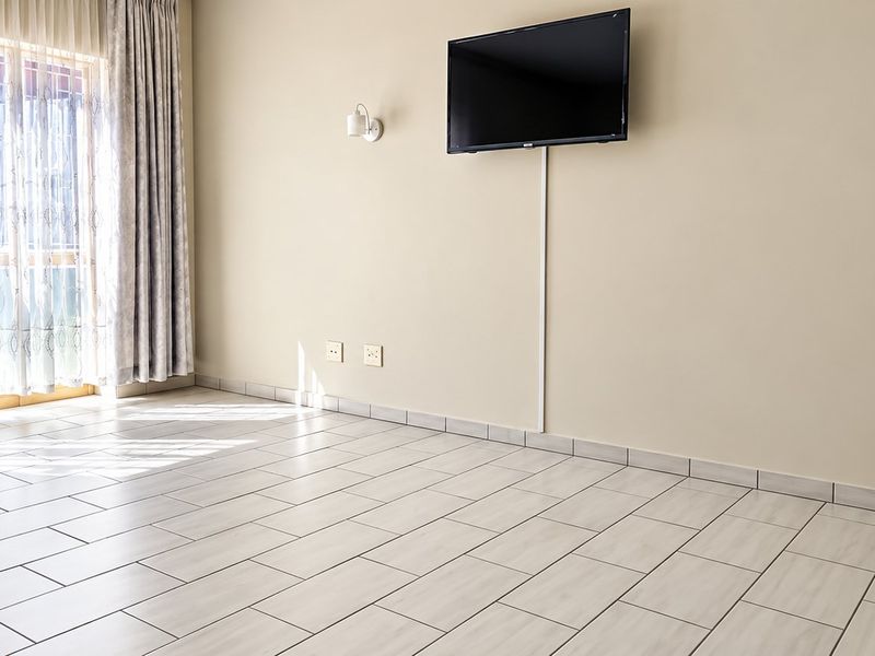 A bright, empty living room featuring neutral tiled flooring, wall-mounted lighting, and large sliding glass doors that provide ample natural light.