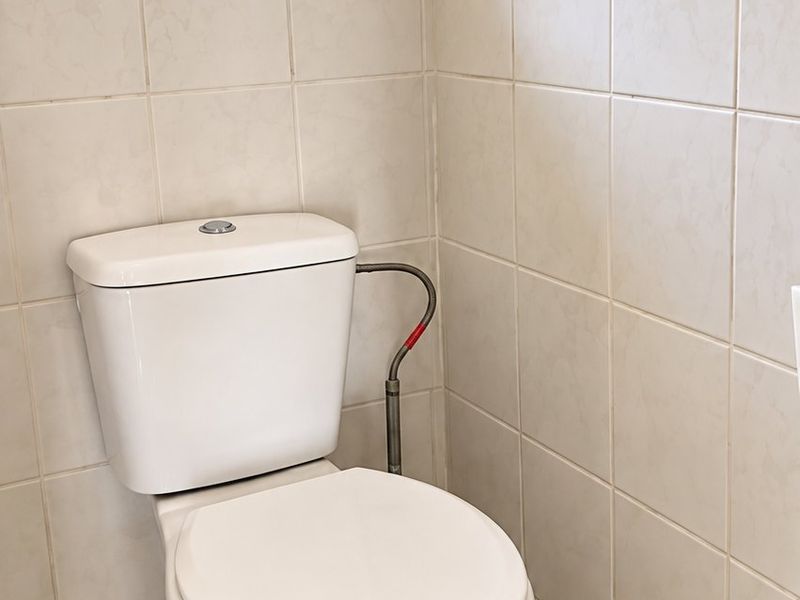 A functional bathroom featuring a standard toilet, neutral ceramic wall and floor tiling, and an obscured glass window for privacy.