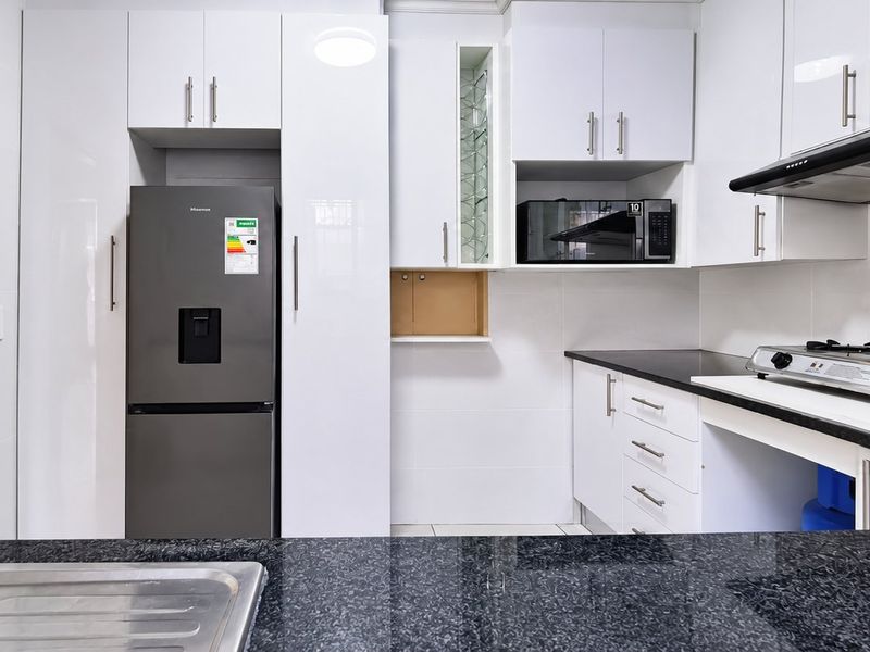 Modern kitchen featuring white high-gloss cabinetry, dark granite countertops, a gas hob with extractor fan, and an adjacent staircase.
