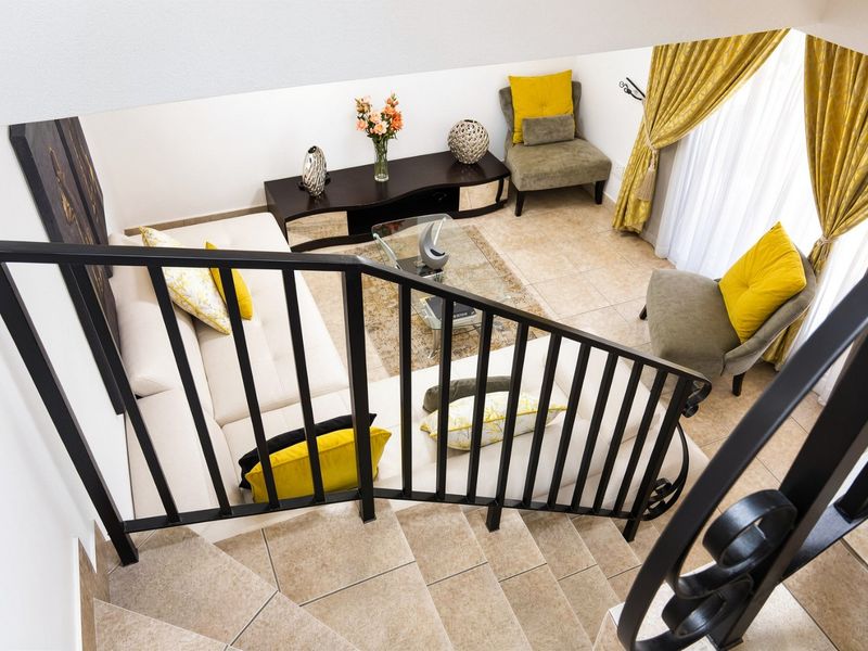 A view from the staircase looking down into a bright, tiled living room area with neutral walls and large window treatments.